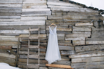 Grey wedding dress hanging on the wooden wall next to wooden ladder