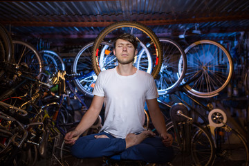 Fototapeta na wymiar Young man is practicing yoga in garage with many bicycles behind him
