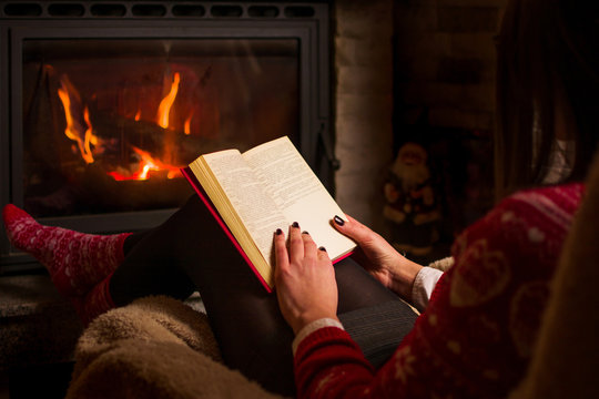 Female reading a book by the fireplace