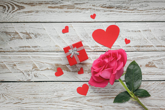 Rose with red paper hearts and gift box on white wooden background. Love symbol concept.