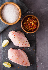 Fresh chicken breast with spices on a stone board, top view copy space.