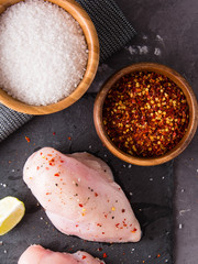 Fresh chicken breast with spices on a stone board, top view copy space.