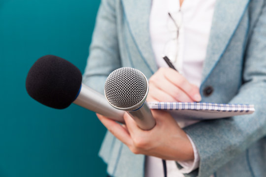 Female journalist at press conference, writing notes, holding microphone