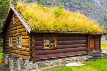 Traditional norwegian wooden house standing on a lawn and mountains in the background. Typical norwegian house with grass on the roof. Flam Norway.