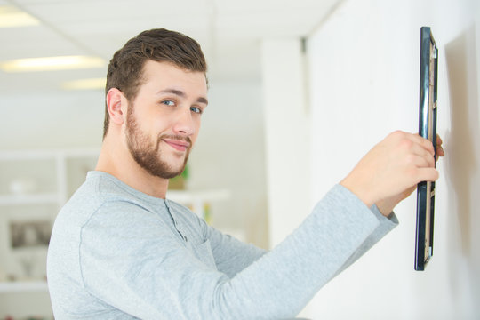 man putting picture frame onto wall