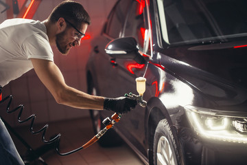 man wear protective mask and eyewear at work. Automobile industry. Car wash and coating business with ceramic coating polishing. Spraying varnish to car.