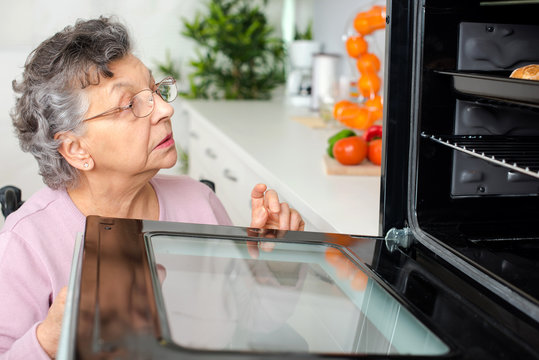senior caucasian woman opening oven in kitchen
