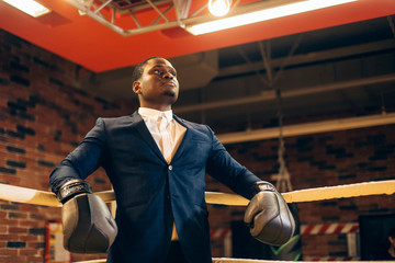 Stock image of person wearing business suit and boxing gloves. African man in a classic suit and...
