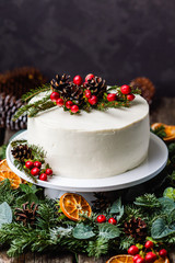 Homemade white cream naked cake decorated with white cream, cones and red berries.