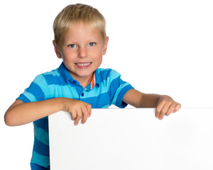 A little boy is looking from behind an empty banner.
