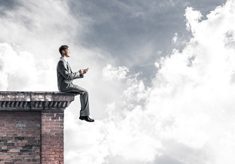 Man on roof edge send message with smartphone and cityscape at b