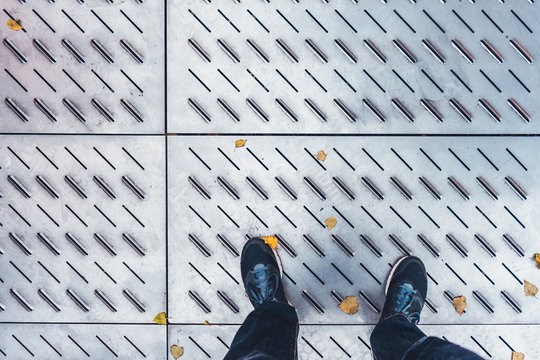 man looking down to his black shoes on steel ground