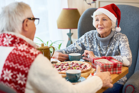 Portrait of loving senior couple celebrating Christmas together sitting at dinner table enjoying meal and talking, focus on elderly  woman wearing Santa hat
