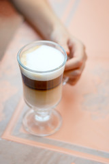 The girl sitting at the table inderjit a glass of latte.