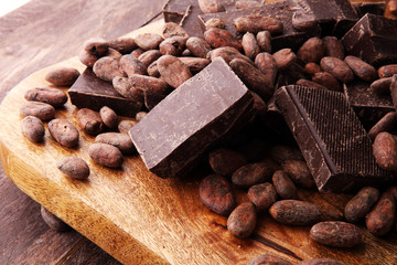 Dark chocolate pieces, stacks and cocoa beans, culinary background.