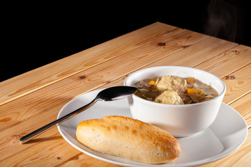 Chicken stew with dumplings and bread roll. Hot comfort food.