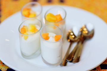 four delicious white dessert souffle with orange fruits on white plate with tea spoons