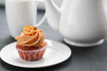 A teapot, a cup of tea and a caramel cupcake.