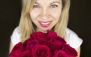 Beautiful blonde, blue eyed woman looking at the camera, smiling with a bouquet of red roses