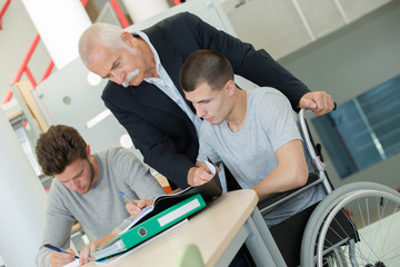 Obraz premium Teacher looking over students' shoulder, one in wheelchair