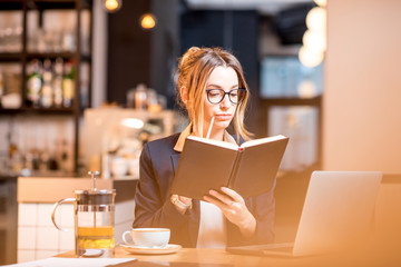 Young businesswoman strictly dressed in the suit working with notebook and laptop at the modern cafe interior. Image with blink effect