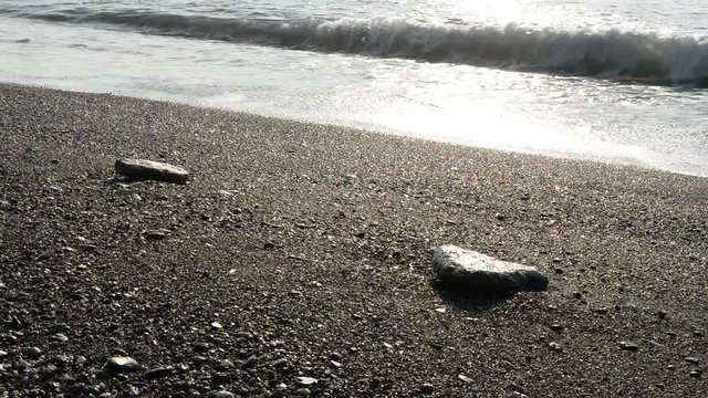 Onde del mare investono sassi sulla spiaggia nelle prime lucu della giornata una estiva