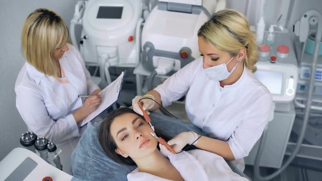 Cosmetologist makes the procedure microcurrent therapy of the facial skin of a beautiful, young woman in a beauty salon