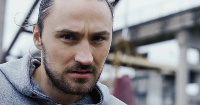 Close up of the young man with aggresive look posing in front of the camera with boxing moves on the cold grey morning. Outdoor. Portrait. Slums on the background