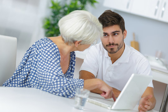young man explaining to elderly woman how to use laptop