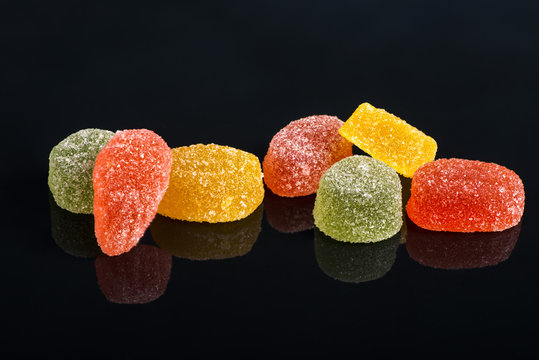 Seven multi-colored fruit-paste sweets  on the black reflecting surface