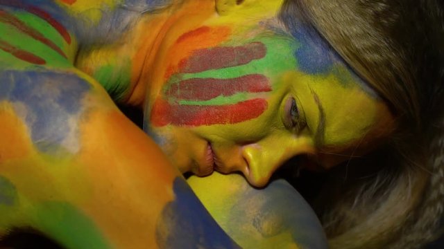 A sad woman in multi-colored body art sits curled