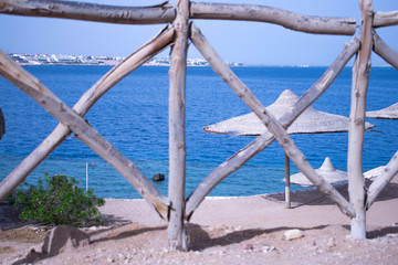 Obraz premium beautiful view of the sea and the blue sky through a wooden fence. wooden umbrellas. vacation in exotic countries. Egypt