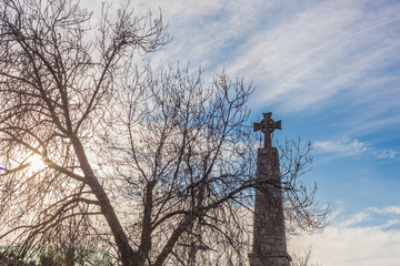 Cemetery crucifix with dry autumn twigs sun and sky to background