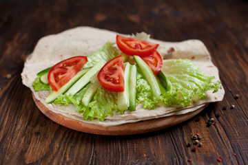  burrito with greens, cucumbers, tomatoes and sausages on a round wooden board on a wooden background