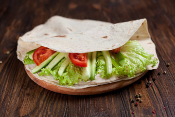  burrito with greens, cucumbers, tomatoes and sausages on a round wooden board on a wooden background