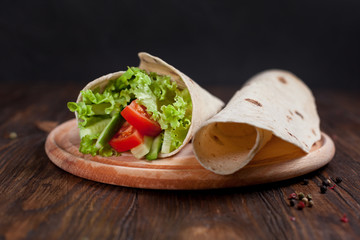  burrito with greens, cucumbers, tomatoes and sausages on a round wooden board on a wooden background