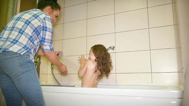 Mother washes the head of a small child. Mom washing her baby with shampoo in a bubble bath. Kid is happy when his mother pours water on his head.
