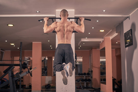 one young bodybuilder, rear view, exercise pull-up bar, gym indoors. full lenght shoot.