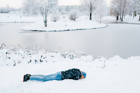Weird odd bizarre unrecognizable male person lying in snow. Man hiding face under snow. Crazy unusual foolish guy freezing himself. Young boy in winter clothes sleeping outdoor in frost cold day.