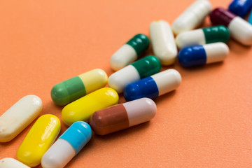 Heap of assorted colorful capsules on orange background.