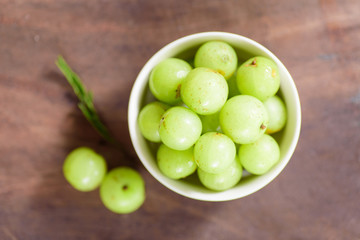 Top view of Indian gooseberry fruit in a bowl on wooden background