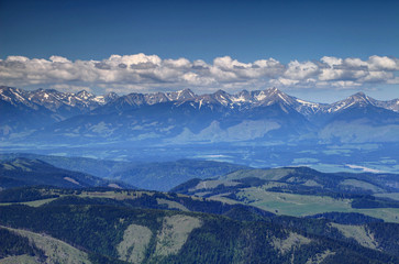 Forested hills and mountains with snow patches in Liptov region Vah valley with white cumulus clouds in a sunny day in spring, Jakubina, Klin, Bystra peaks, Zapadne Tatry, Carpathians, Slovakia Europe