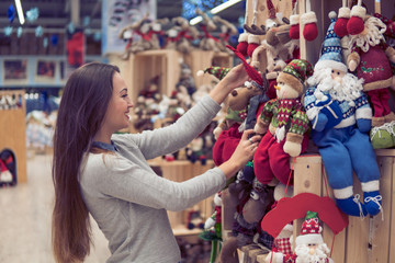Fototapeta na wymiar Cheerful happy customer girl choosing gifts for Christmas and New Year. She is holding New Year's deer and Santa Claus toys