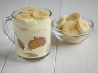 Glass bowl with pieces of banana and banana pudding in a Cup on a white table.