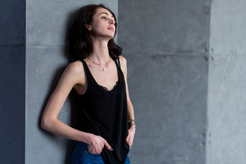 Skinny young European female model in casual clothes posing standing relaxed leaning on wall looking away from camera