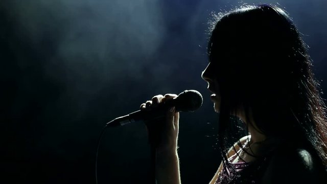 Silhouette of a beautiful girl singer with microphone in the dark.