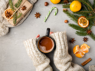 Obraz na płótnie Canvas Winter hot drink female hands in a sweater holding a Cup of hot chocolate on a gray concrete background tangerines scenery