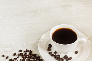 Black coffee in white cup and coffee beans on soft wooden background.