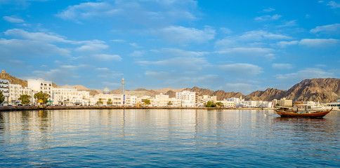 Muscat Skyline with a traditional arabic Dhow anchored at the port - obrazy, fototapety, plakaty