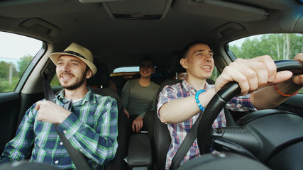 Group of happy friends in car singing and dancing while drive road trip